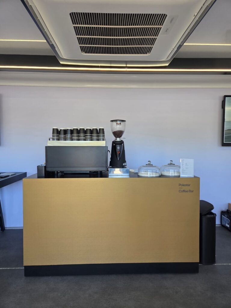 Gold Polestar-branded coffee bar by Tom’s Coffee with espresso machine, grinder and stacked cups at a Polestar brand activation