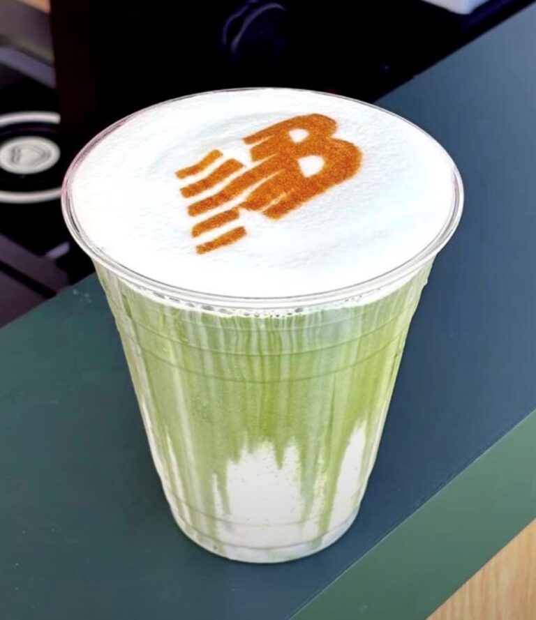 Matcha latte in a branded cup with a logo stencilled onto the foam